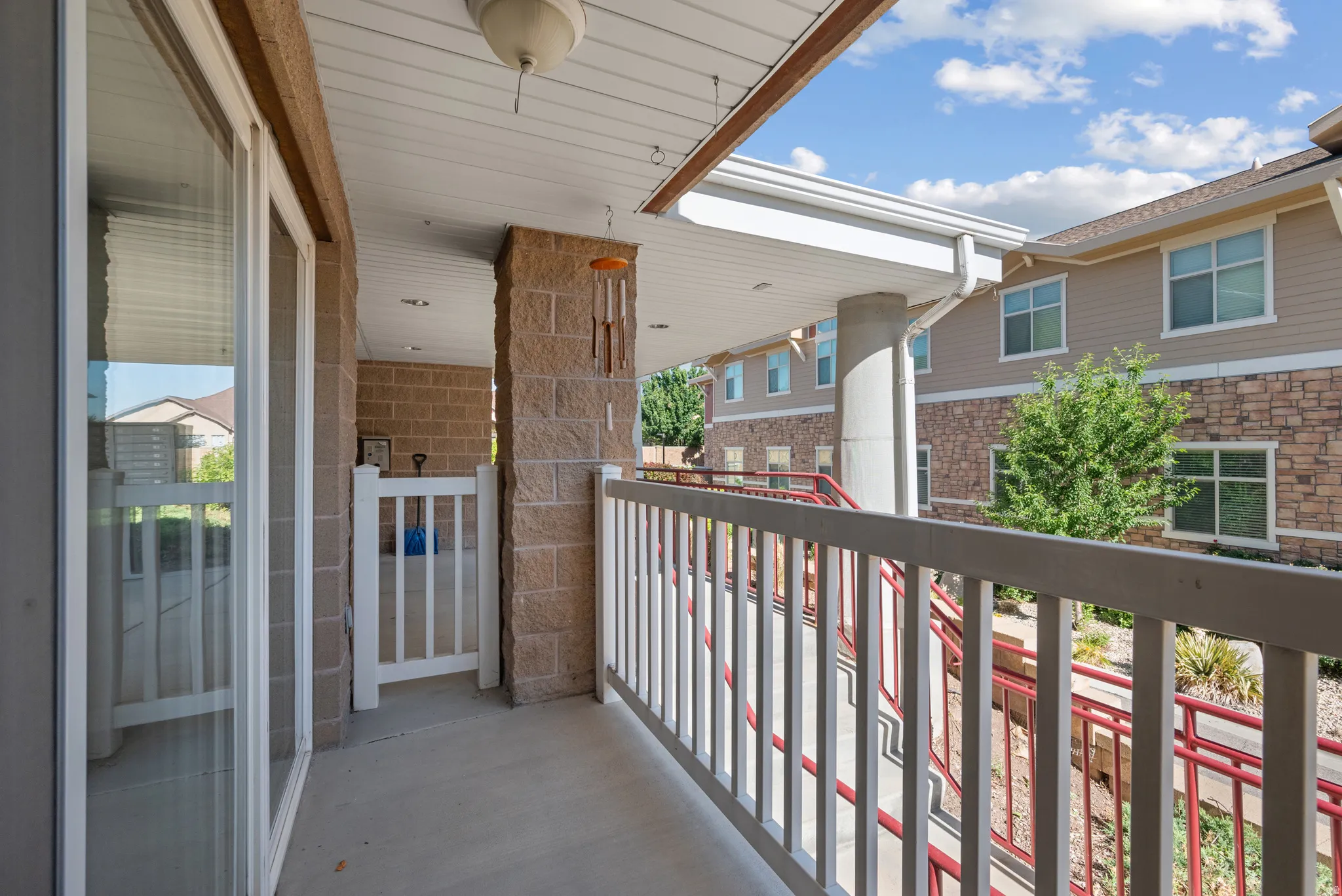 Covered patio featuring a concrete floor, stone veneer accents, white railing, and a sliding glass door