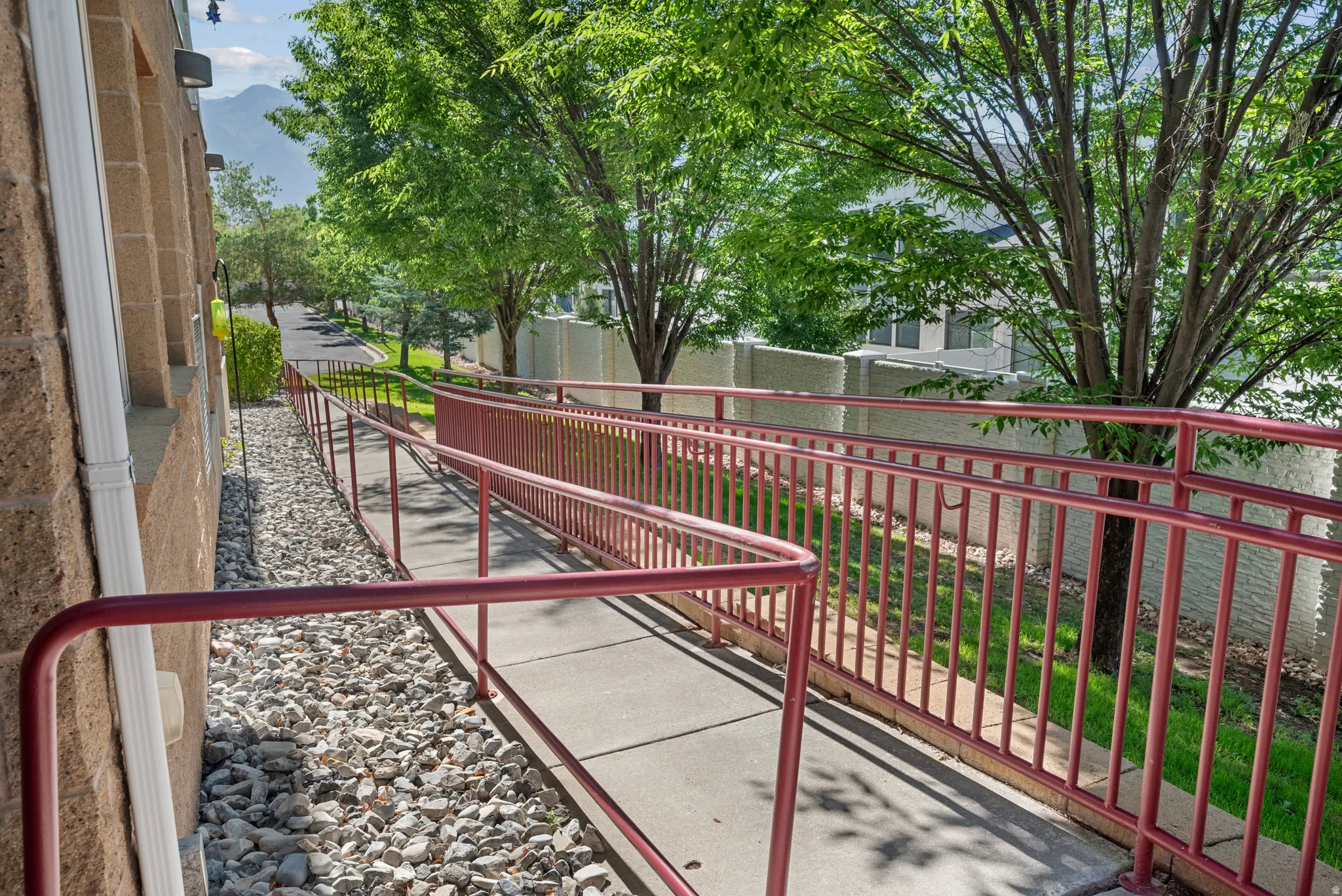Concrete ramp with red metal railings, textured block exterior, white downspout, and gravel landscaping