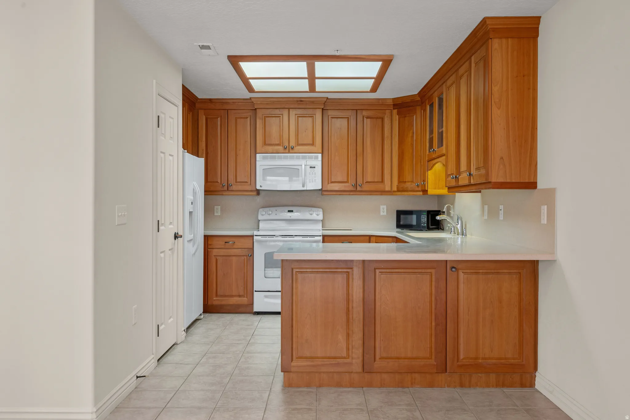 Kitchen featuring wood-finish cabinetry, white appliances, light-toned countertops, and tile flooring