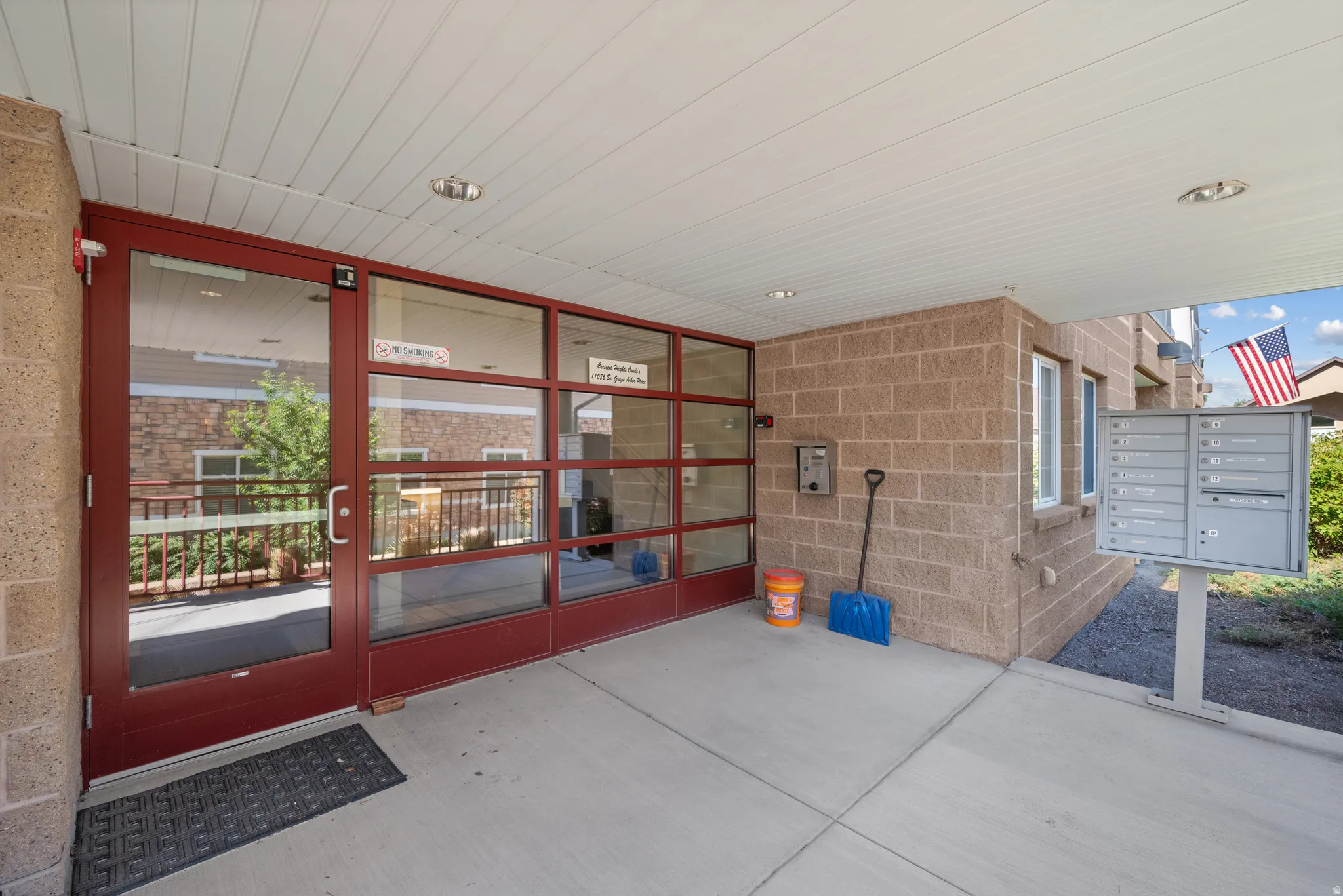 Covered concrete entryway featuring a red-framed glass door, brick facade, and wall-mounted mailboxes