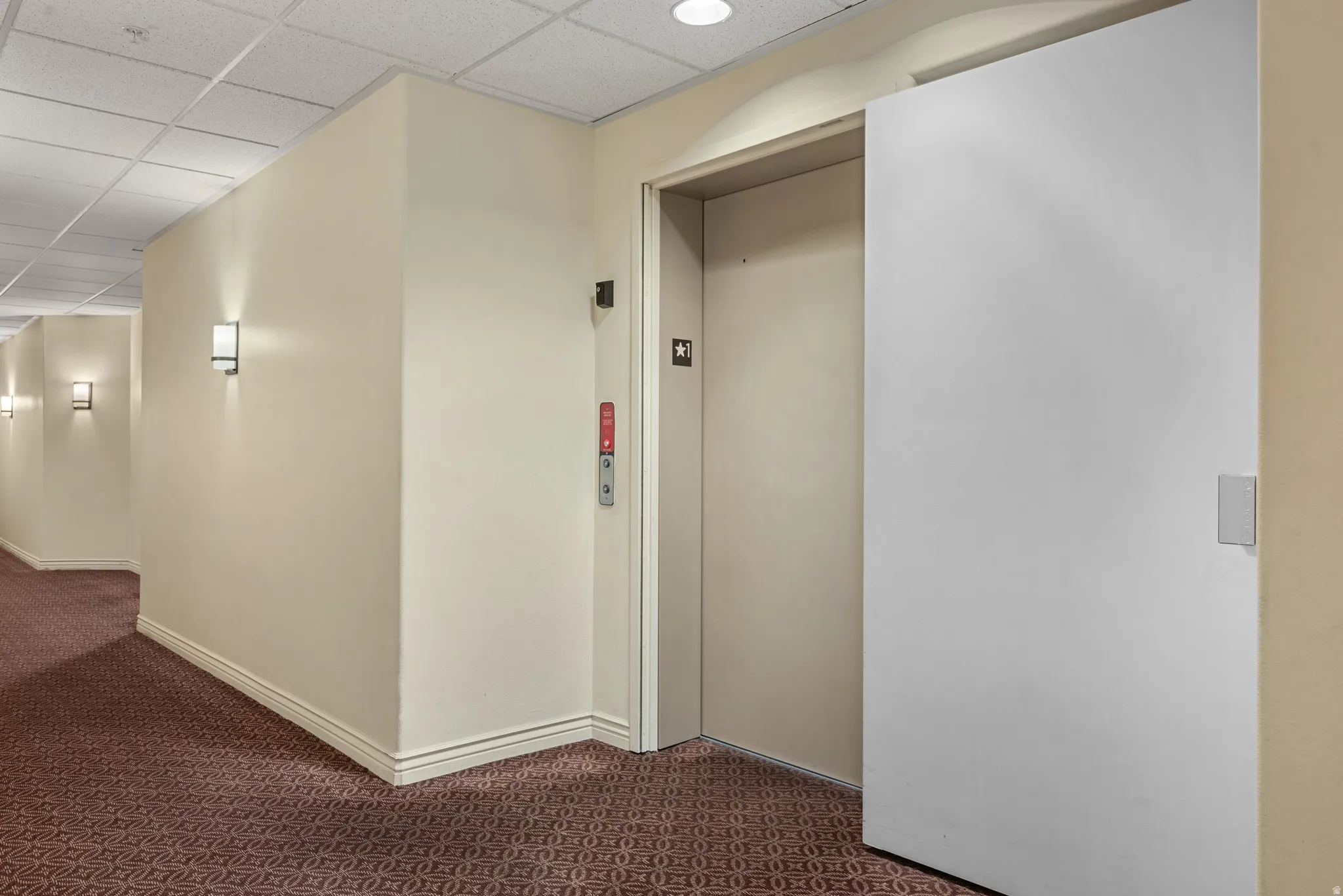 Elevator access featuring neutral wall tones, decorative sconce lighting, and patterned carpet flooring