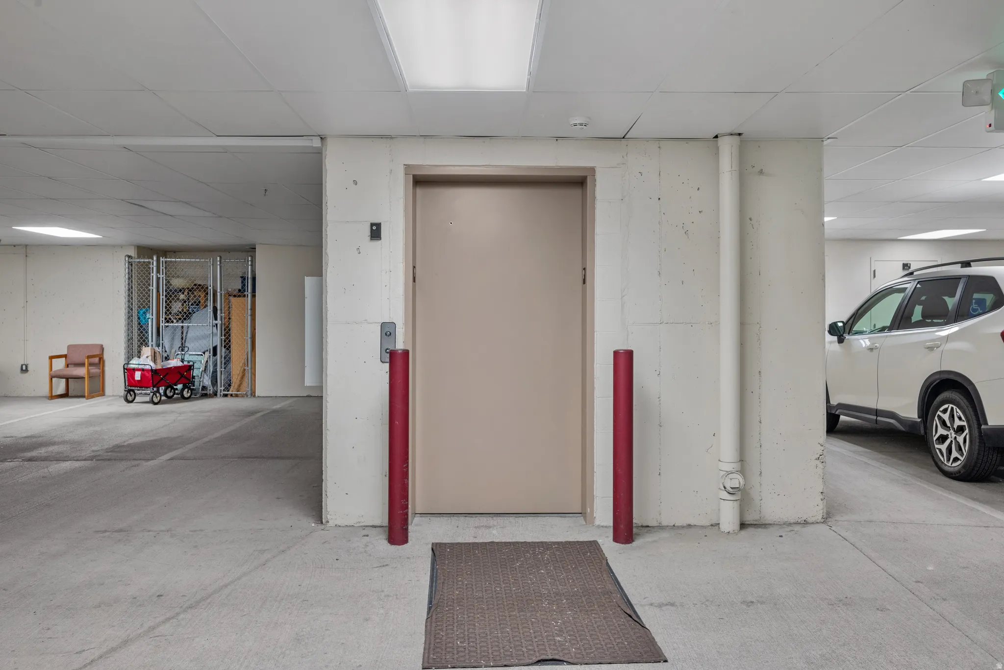 Garage parking space with concrete flooring, illuminated by overhead fluorescent lighting, featuring an elevator access point