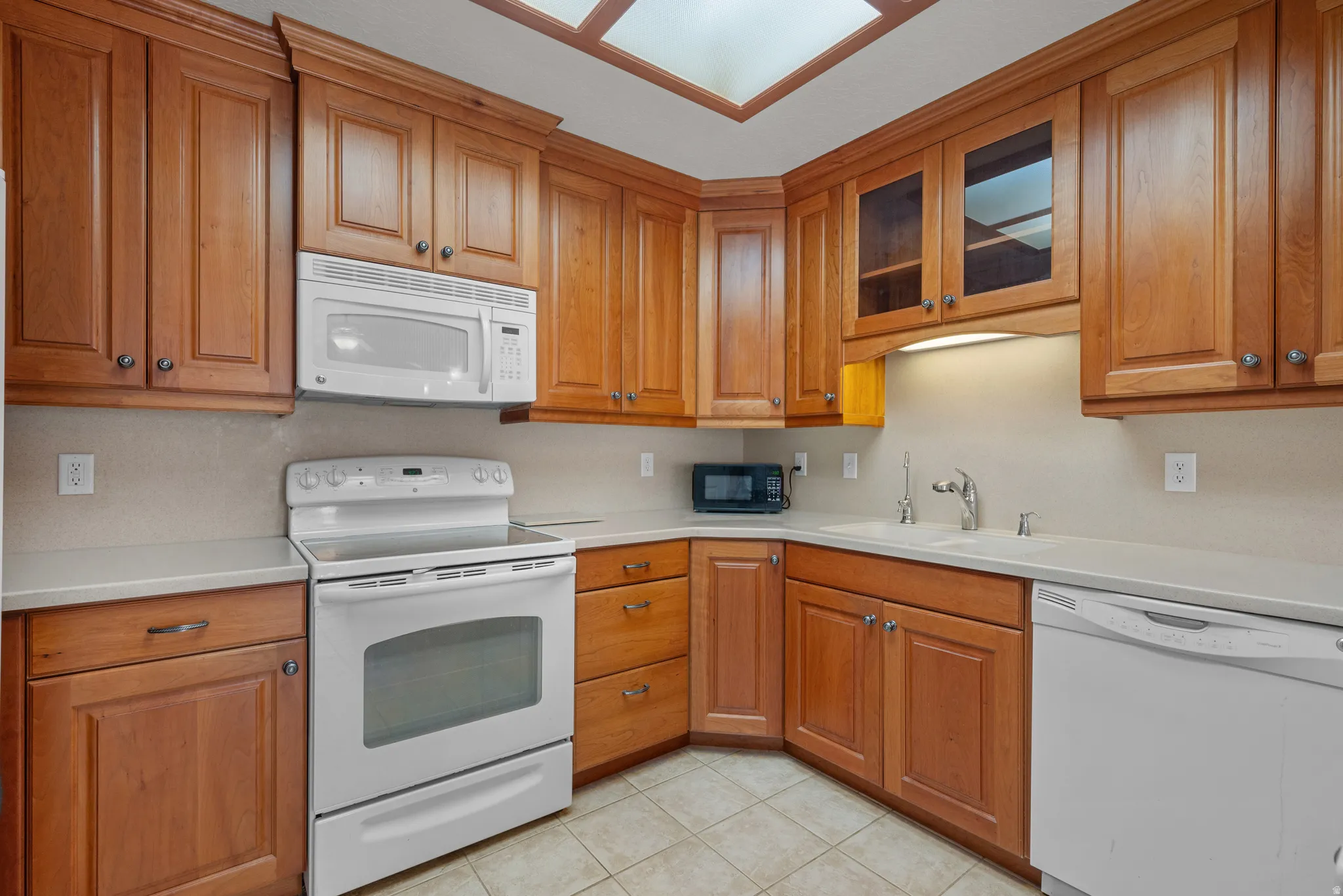 Kitchen featuring abundant wood cabinetry, white appliances, light countertops, and tile flooring