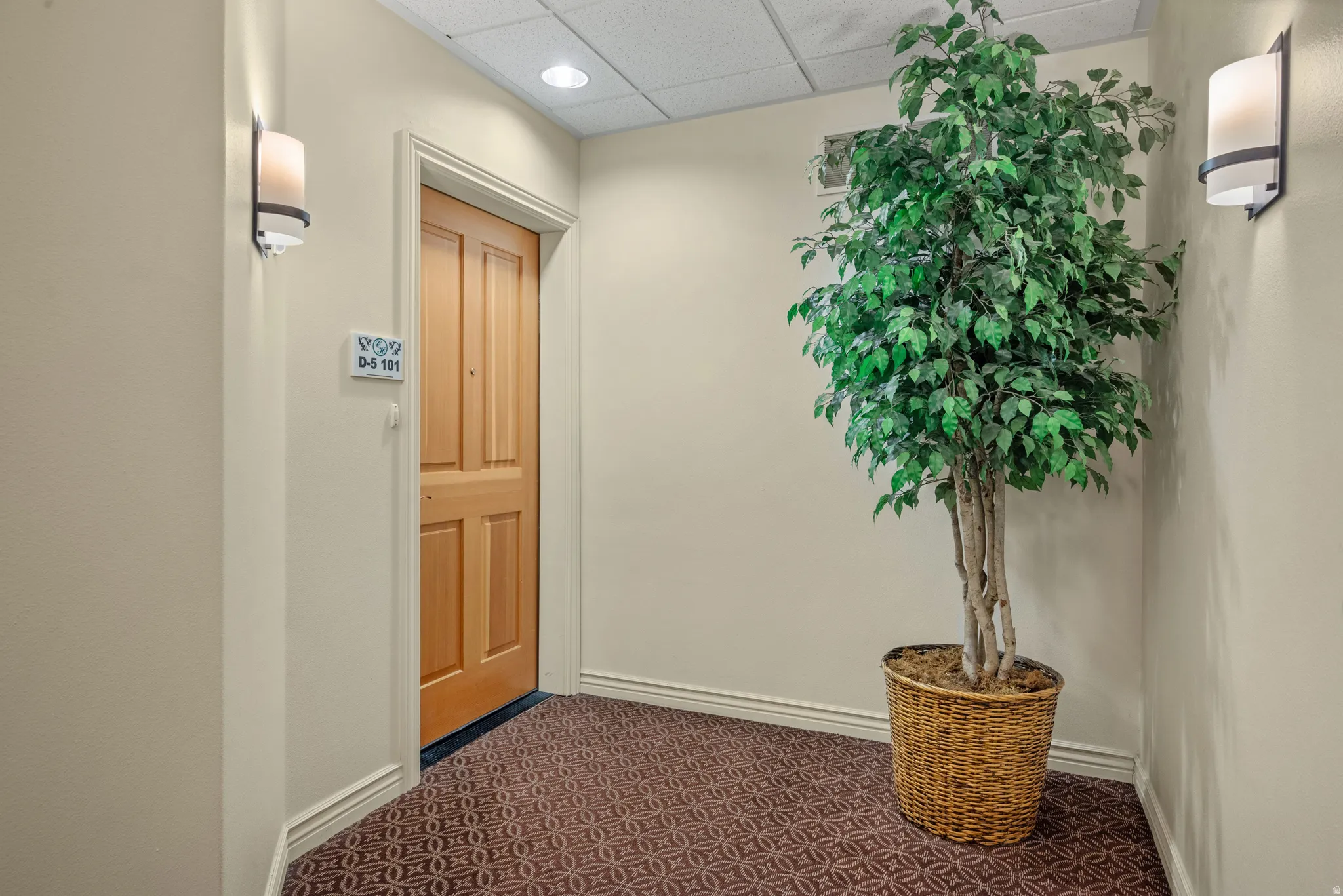 Entryway featuring a paneled wood door, sconce lighting, and patterned carpet flooring