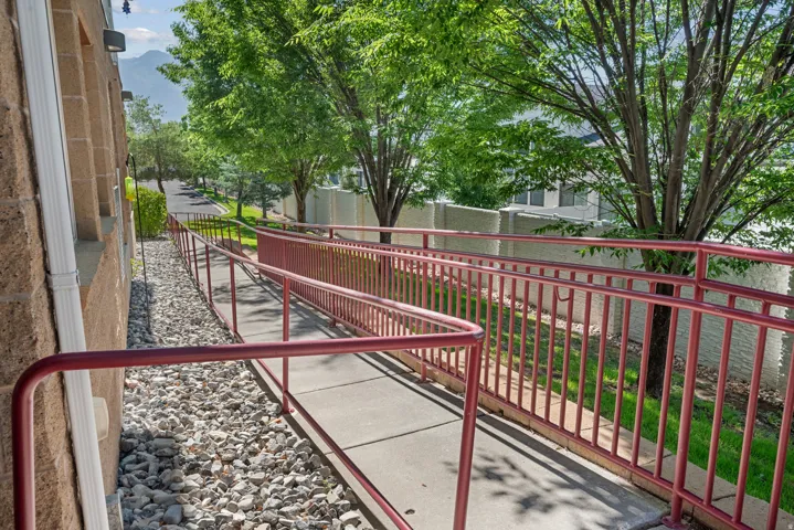 Concrete ramp with red metal railings, textured block exterior, white downspout, and gravel landscaping