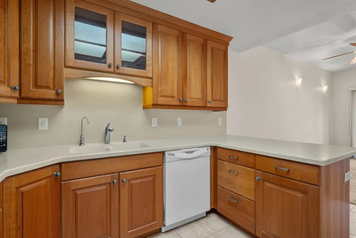 Kitchen featuring wood cabinetry, solid surface countertops, a double basin sink with a gooseneck faucet, an integrated dishwasher, and tile flooring