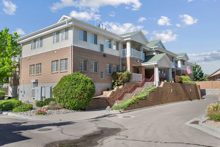 Multi-story building featuring brick and siding facade, multiple balconies with white railings, a green gabled roofline, and an asphalt driveway