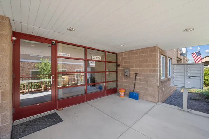Covered concrete entryway featuring a red-framed glass door, brick facade, and wall-mounted mailboxes