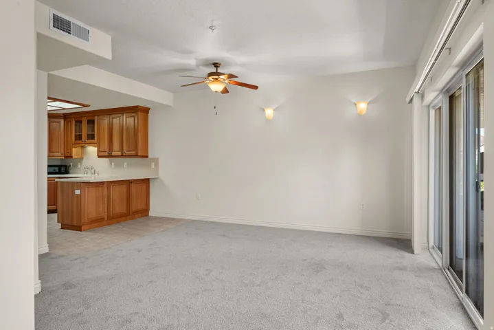 Expansive carpeted living area featuring a ceiling fan with integrated lighting, two wall sconces, and sliding glass doors