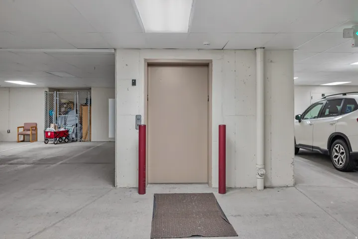 Garage parking space with concrete flooring, illuminated by overhead fluorescent lighting, featuring an elevator access point