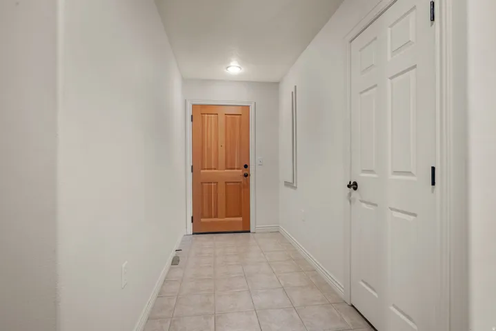 Entryway featuring a natural wood-finish front door with black hardware, complementing paneled interior doors, and neutral tile flooring