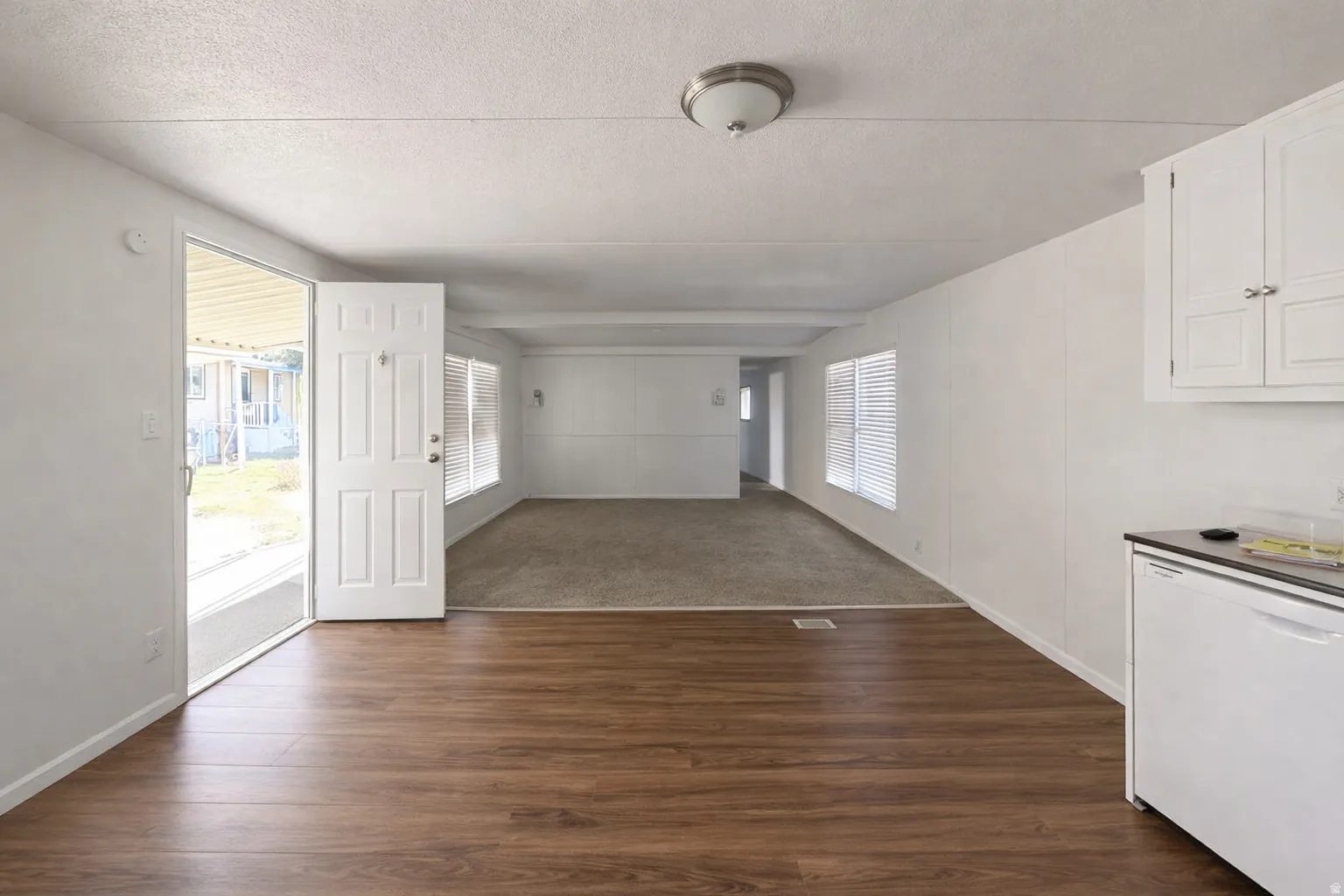 Image from 2 yrs ago before move-in. Open-concept interior featuring wood-finish flooring and white panel walls. Looking from the kitchen over the dining area and into the family room.