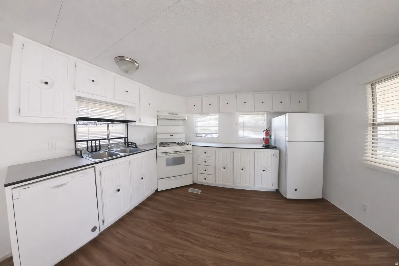 Image from 2 yrs ago before move-in. Kitchen featuring wood-finish flooring, white cabinetry, a double basin sink, and white appliances including a refrigerator, range, and dishwasher