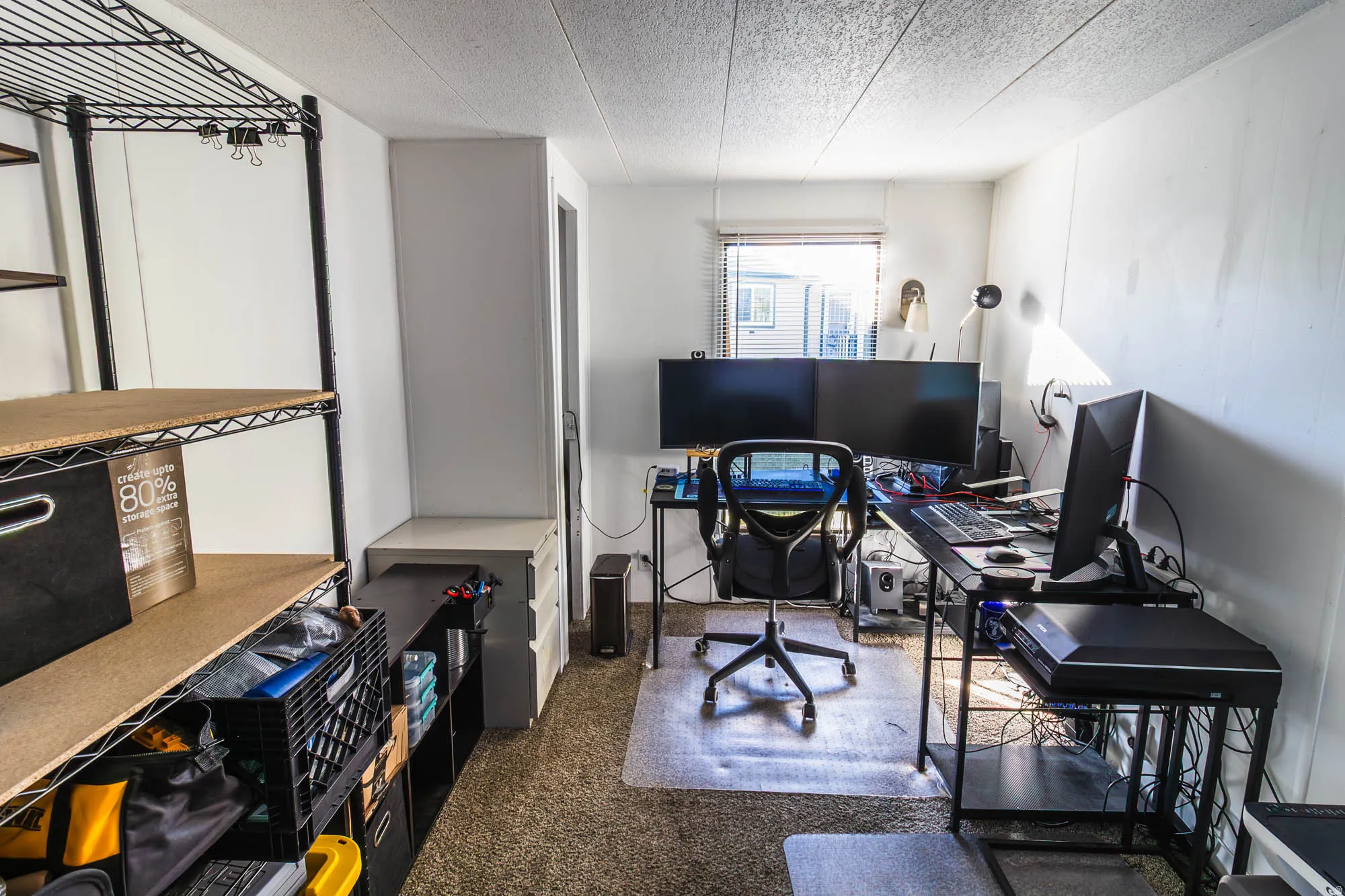 Interior room featuring textured carpeting, white painted walls, a window with blinds, and a built-in countertop with shelving