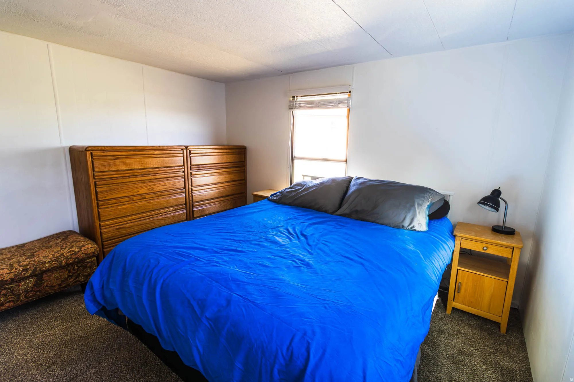 Carpeted bedroom featuring a window with blinds, white panel walls, and a textured ceiling