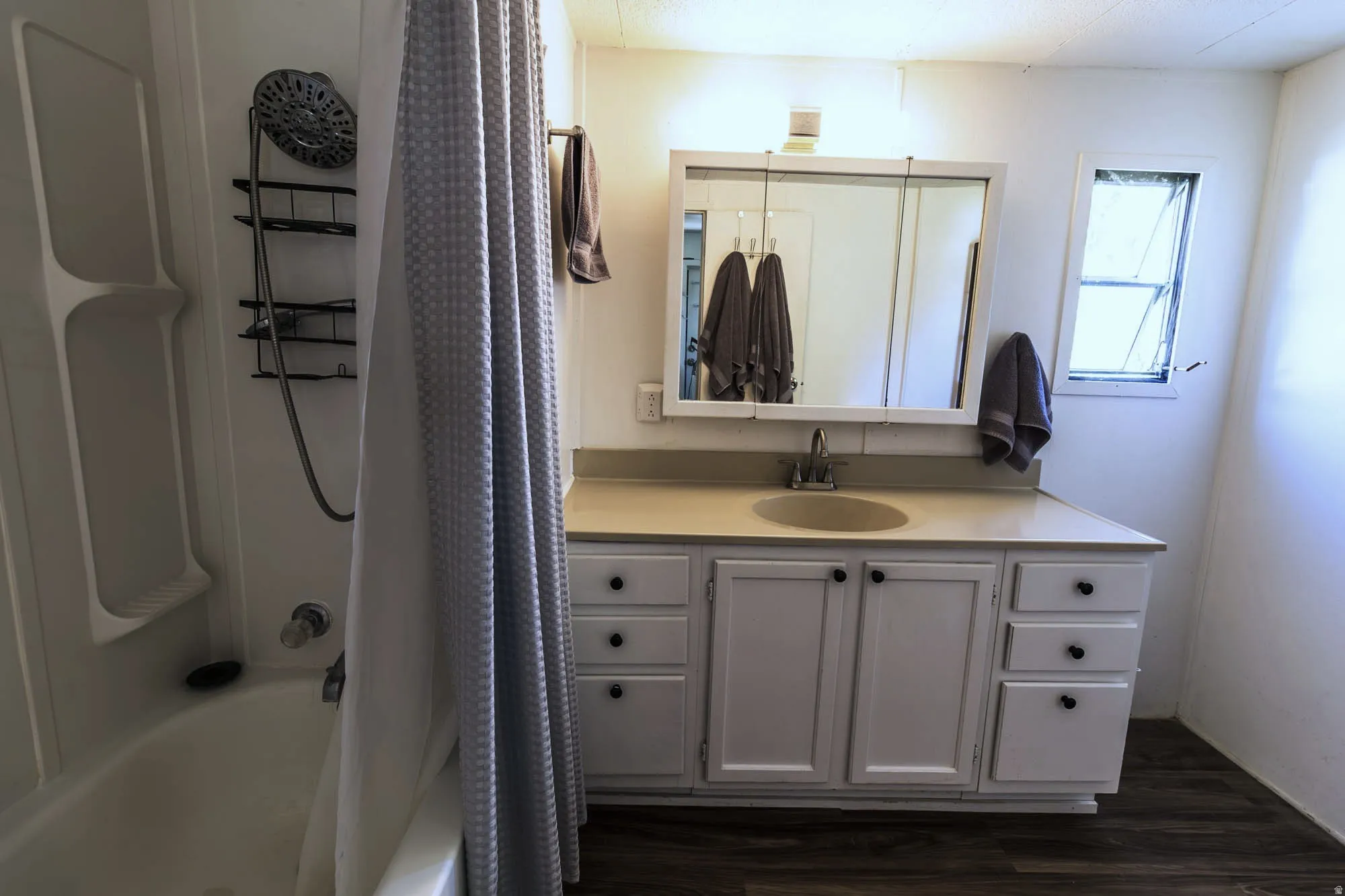 Bathroom featuring a white vanity with integrated sink, a mirrored medicine cabinet, a window with obscure glass, a shower/tub combination, and wood-finish flooring