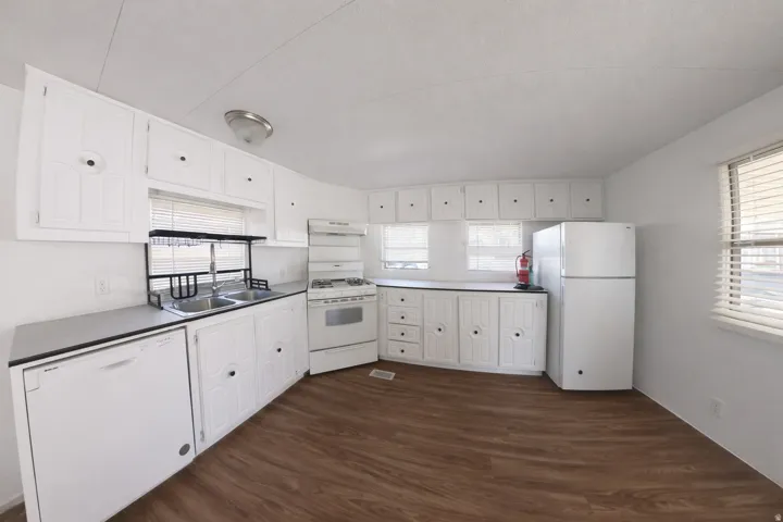 Image from 2 yrs ago before move-in. Kitchen featuring wood-finish flooring, white cabinetry, a double basin sink, and white appliances including a refrigerator, range, and dishwasher