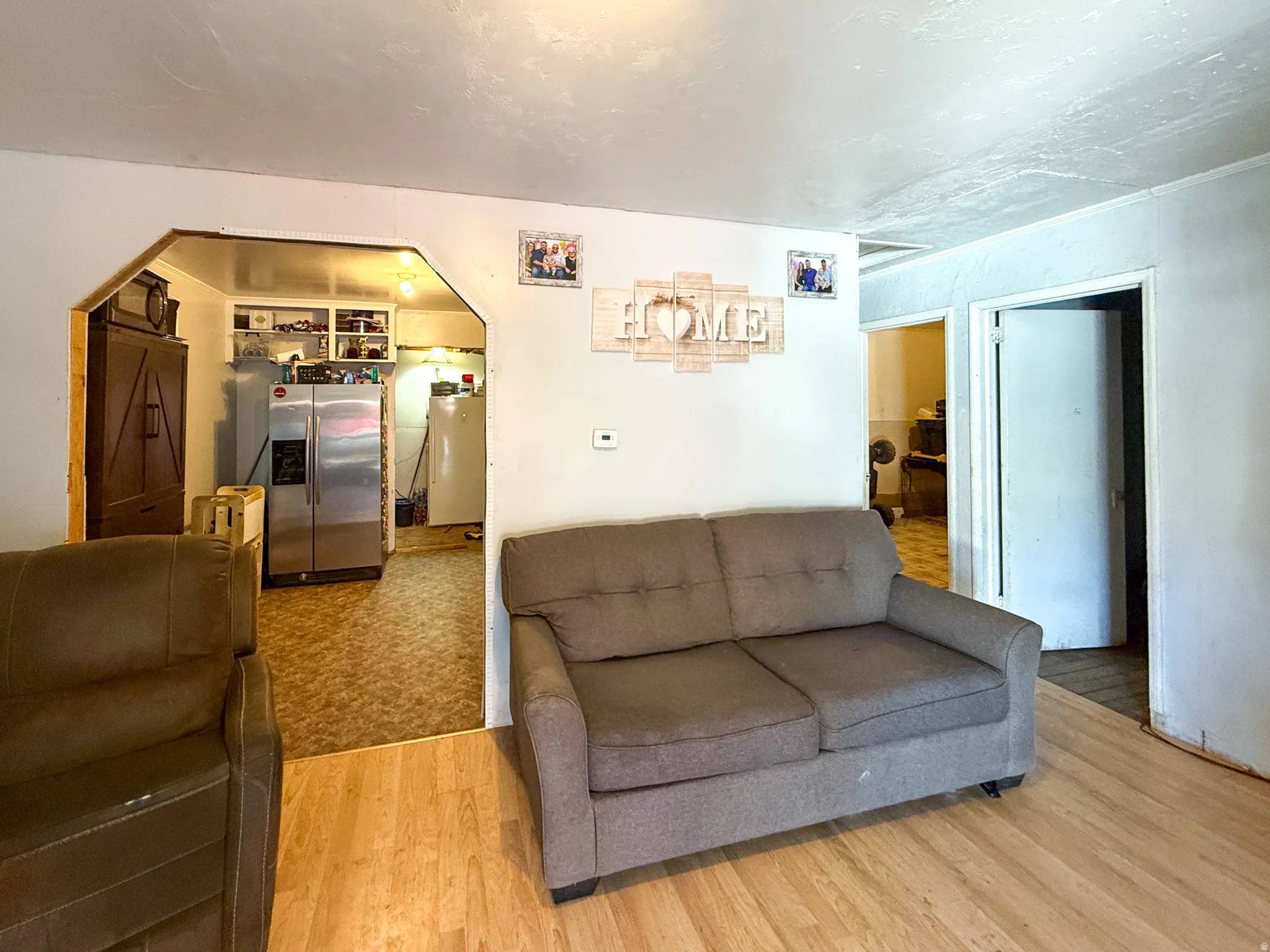 Interior space featuring wood-finish flooring, white walls, and an arched doorway leading to a kitchen with a stainless steel refrigerator