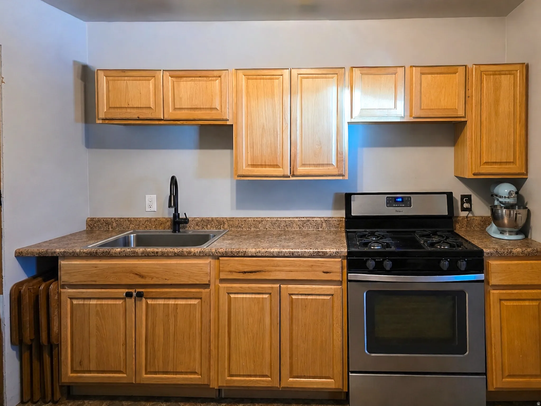 Kitchen area featuring light wood-finish cabinetry, a stainless steel sink with a black faucet, and a stainless steel range with a black cooktop