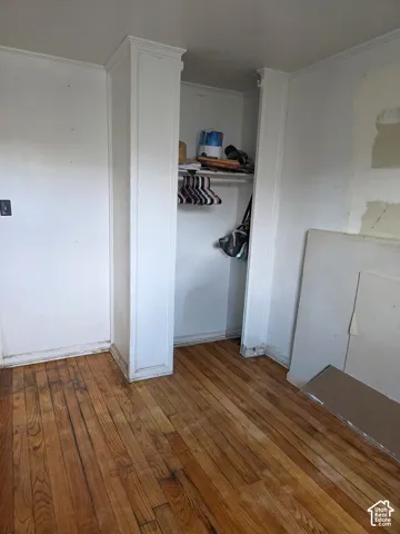 Wood-finish flooring with a built-in closet featuring a clothes rod and storage shelf