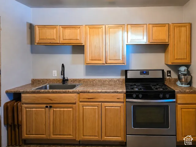 Kitchen area featuring light wood-finish cabinetry, a stainless steel sink with a black faucet, and a stainless steel range with a black cooktop