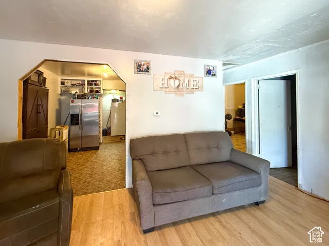 Interior space featuring wood-finish flooring, white walls, and an arched doorway leading to a kitchen with a stainless steel refrigerator