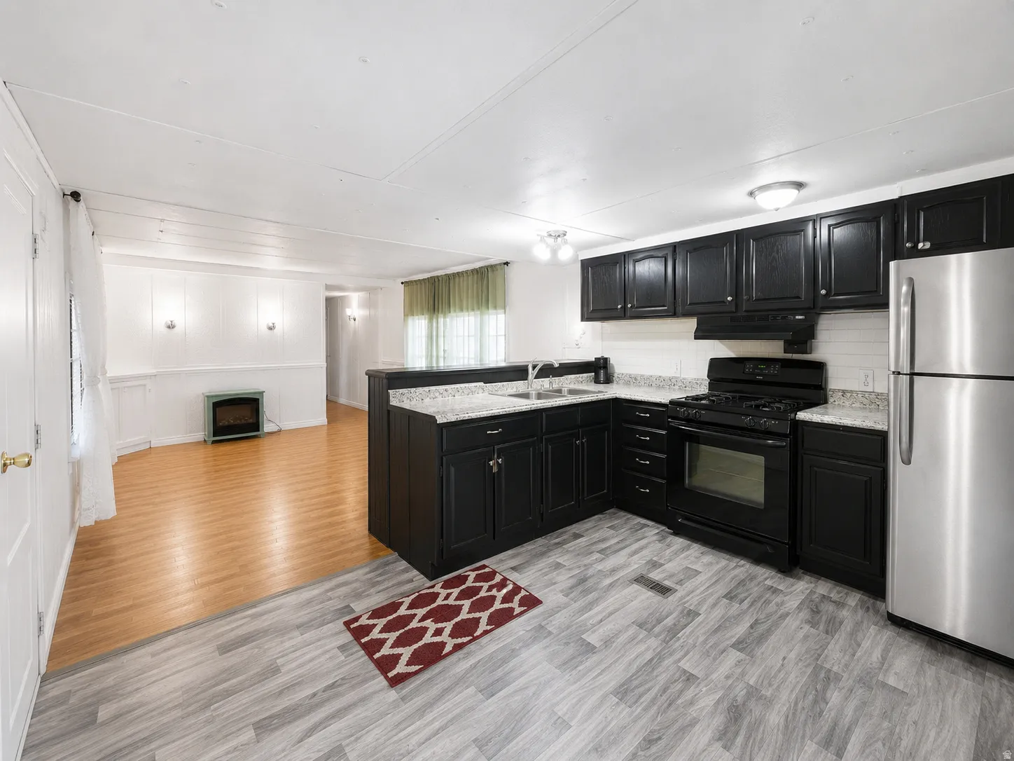 Open kitchen and living area featuring black cabinetry, stainless steel appliances, light countertops, and easy flow into the main living space.