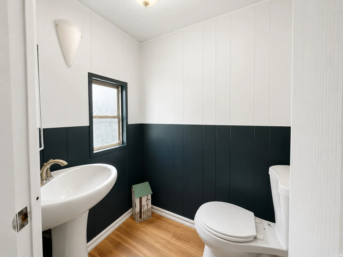 Half bathroom with pedestal sink, two-tone wall detail, and wood-look flooring.