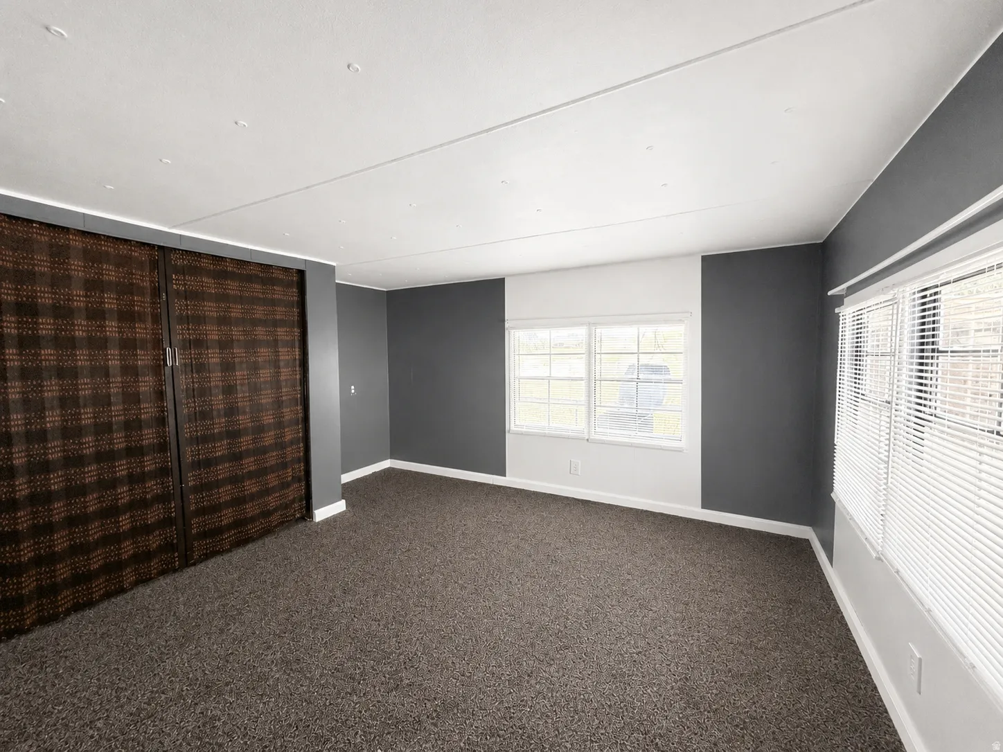Large bedroom with dark carpet, gray accent walls, multiple windows, and generous closet space.