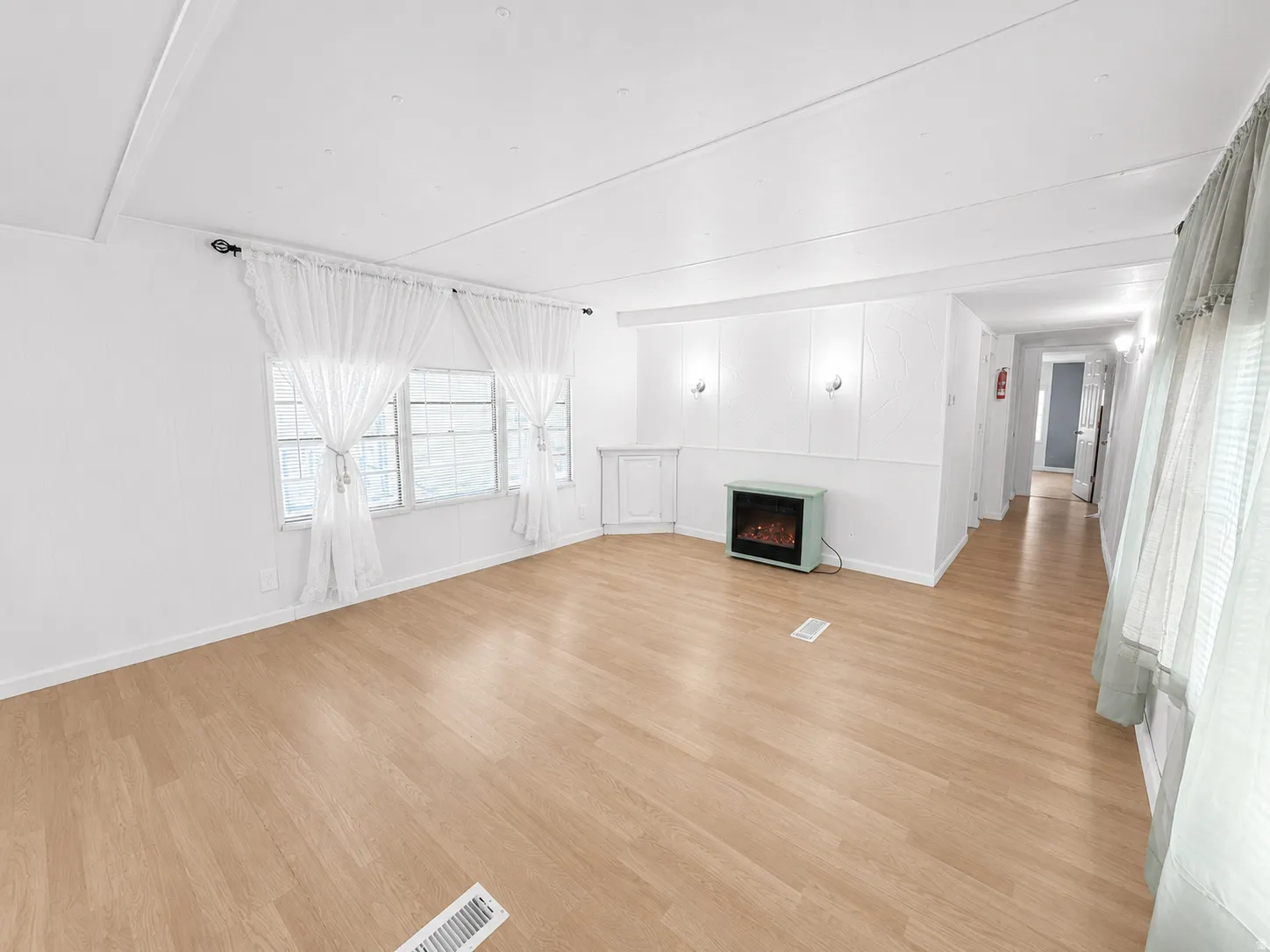 Bright and open living room featuring light flooring, white walls, large windows, and an electric fireplace.
