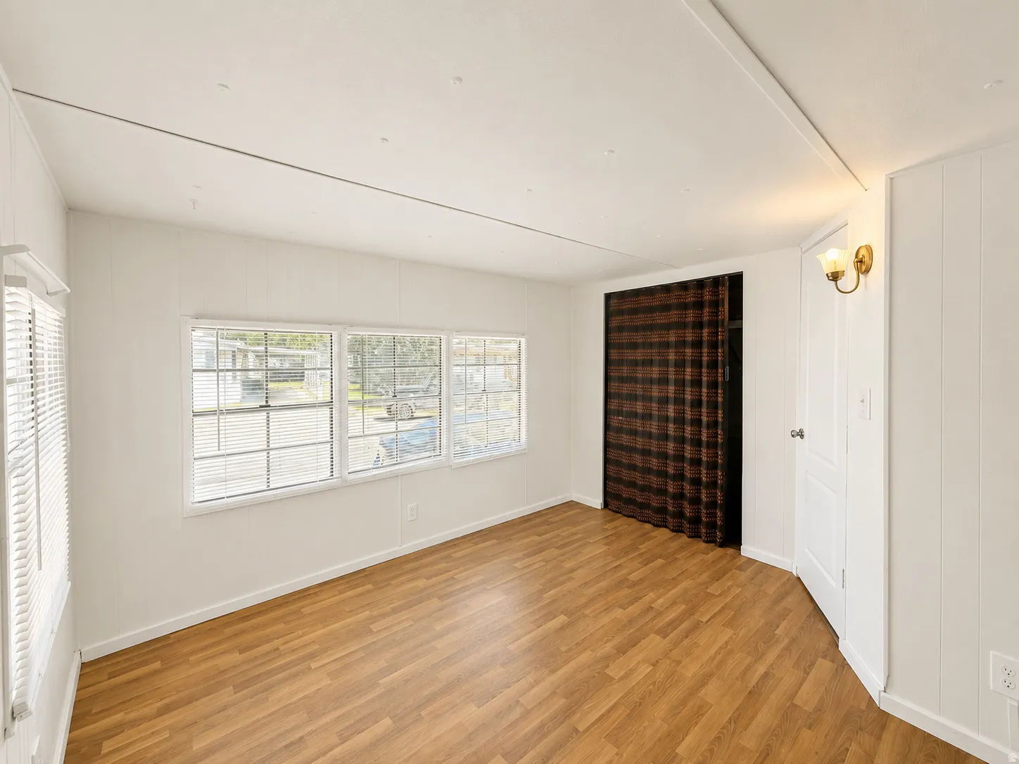 Bright bedroom featuring wood-look flooring, multiple windows, and neutral walls for easy decorating.