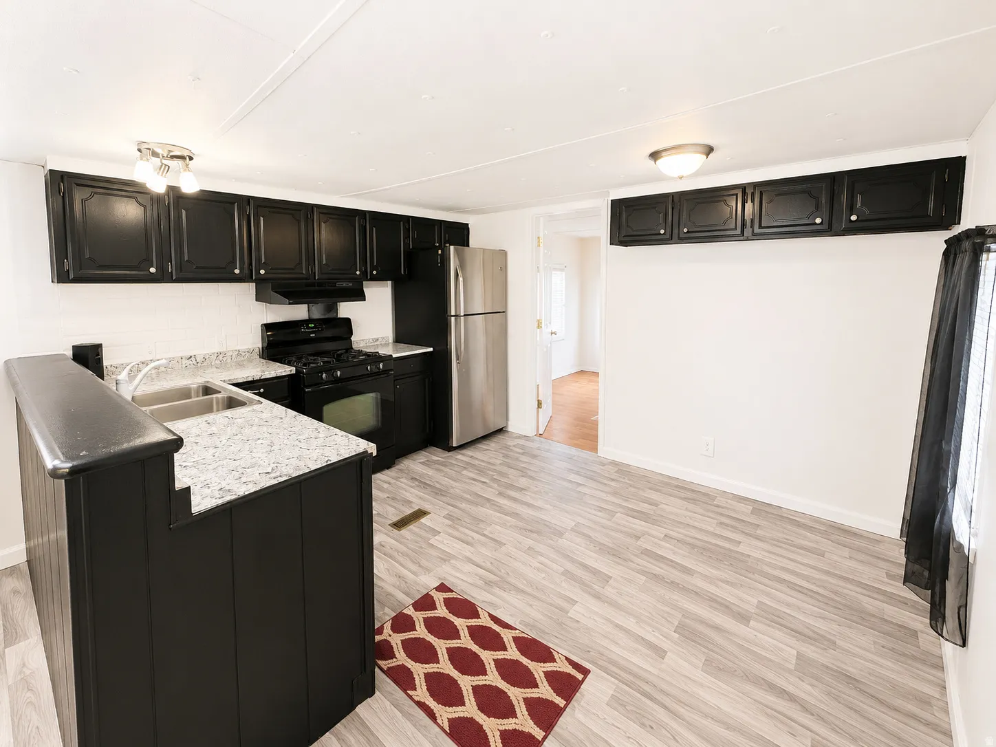 Kitchen view showcasing black cabinetry, stainless steel appliances, light countertops, and open sightline to the living room.