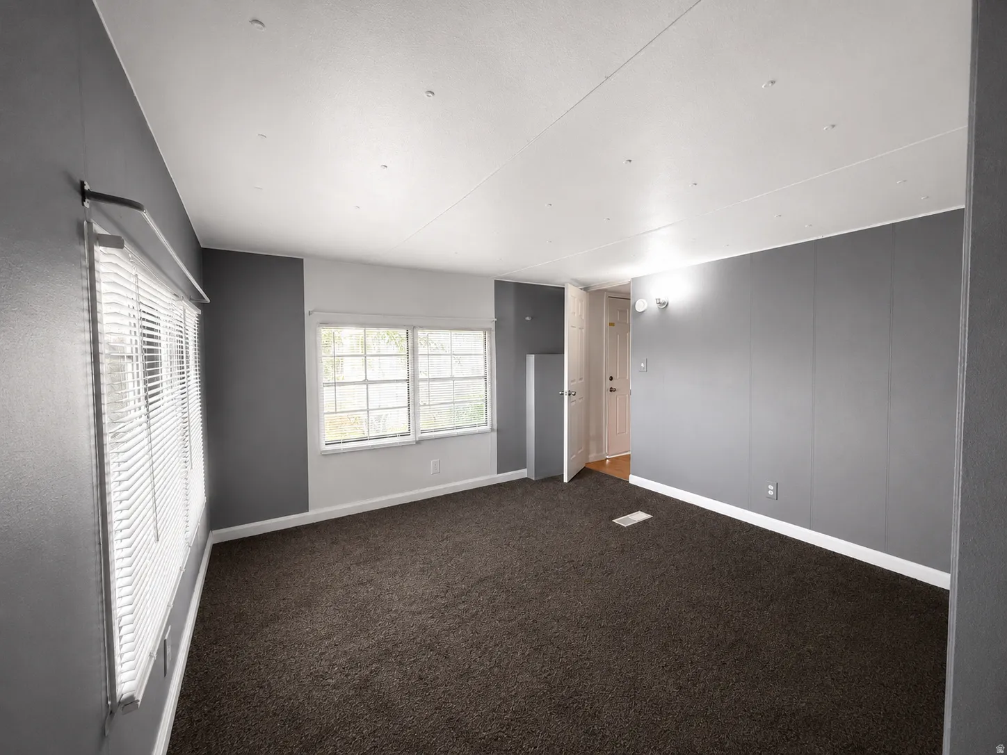 Bedroom view featuring natural light, neutral gray walls, and comfortable carpeted flooring.