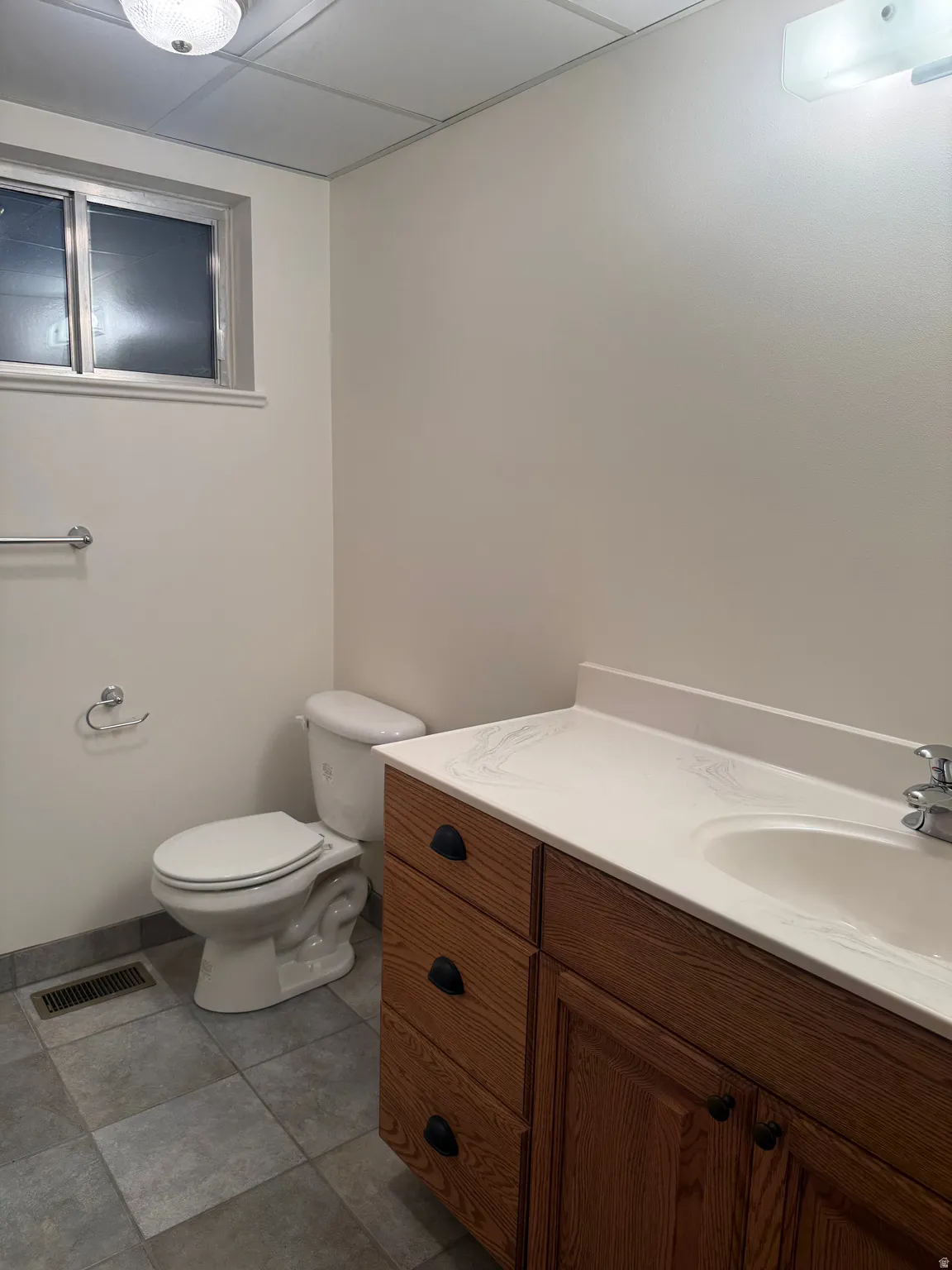 Bathroom featuring a vanity with wood cabinetry, a white countertop with integrated sink, and a commode