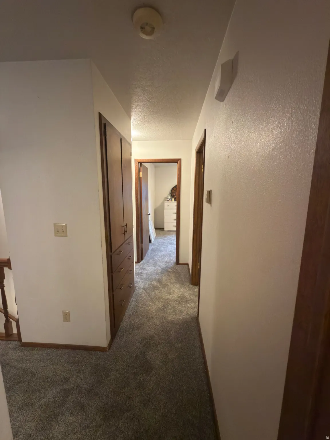 Hallway featuring gray carpeting, white walls, wood trim, and wood built-in cabinetry