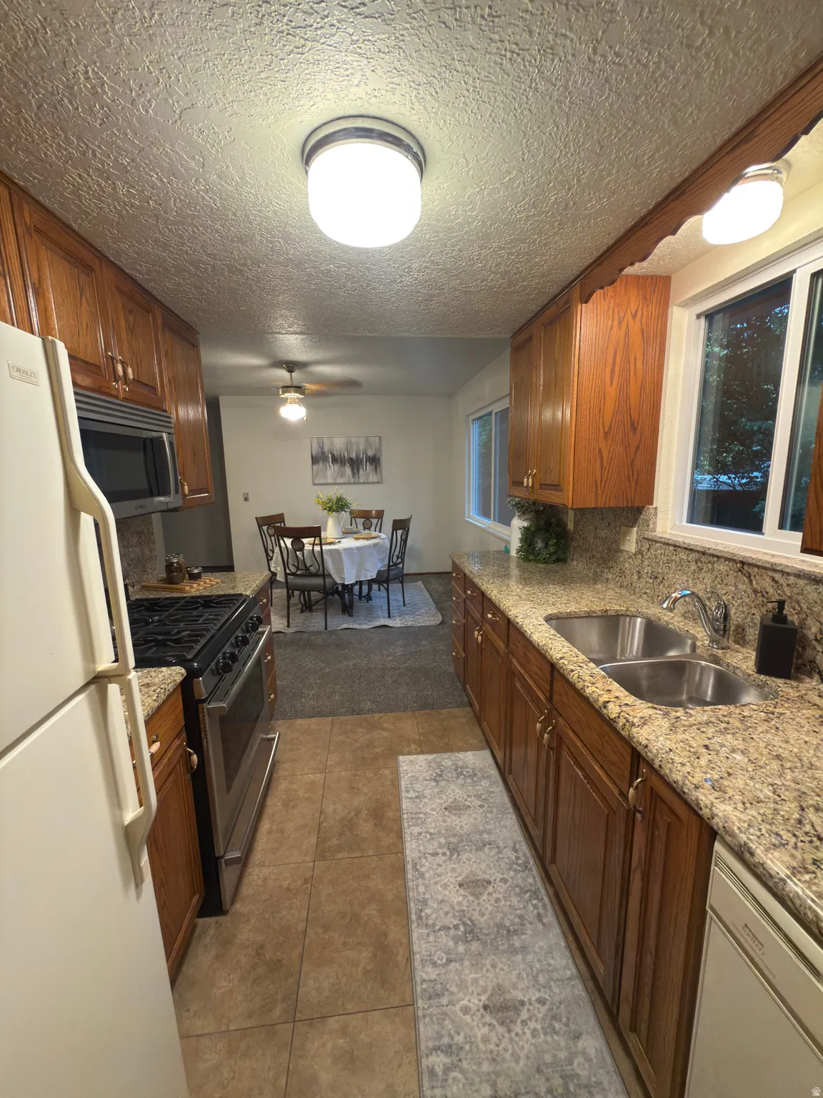 Galley kitchen featuring wood cabinetry, granite-style countertops, and a dual basin stainless steel sink