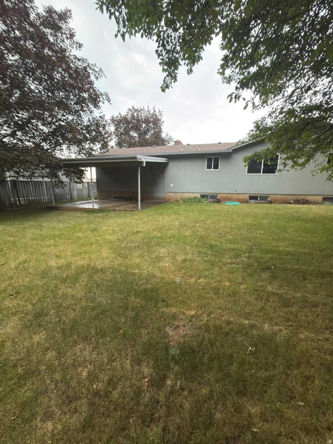 Rear exterior with covered patio, expansive lawn, and mature perimeter trees