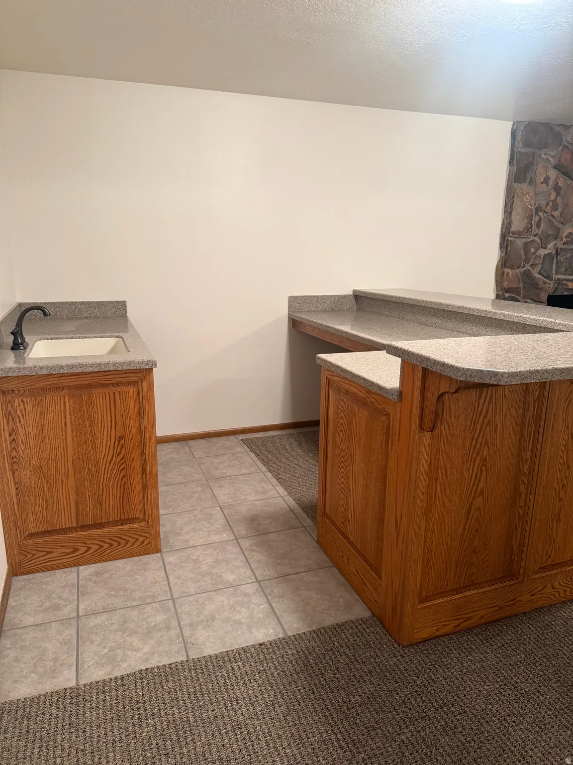 Built-in entertainment bar featuring a tiered countertop, wood-finish cabinetry, and a stone accent wall