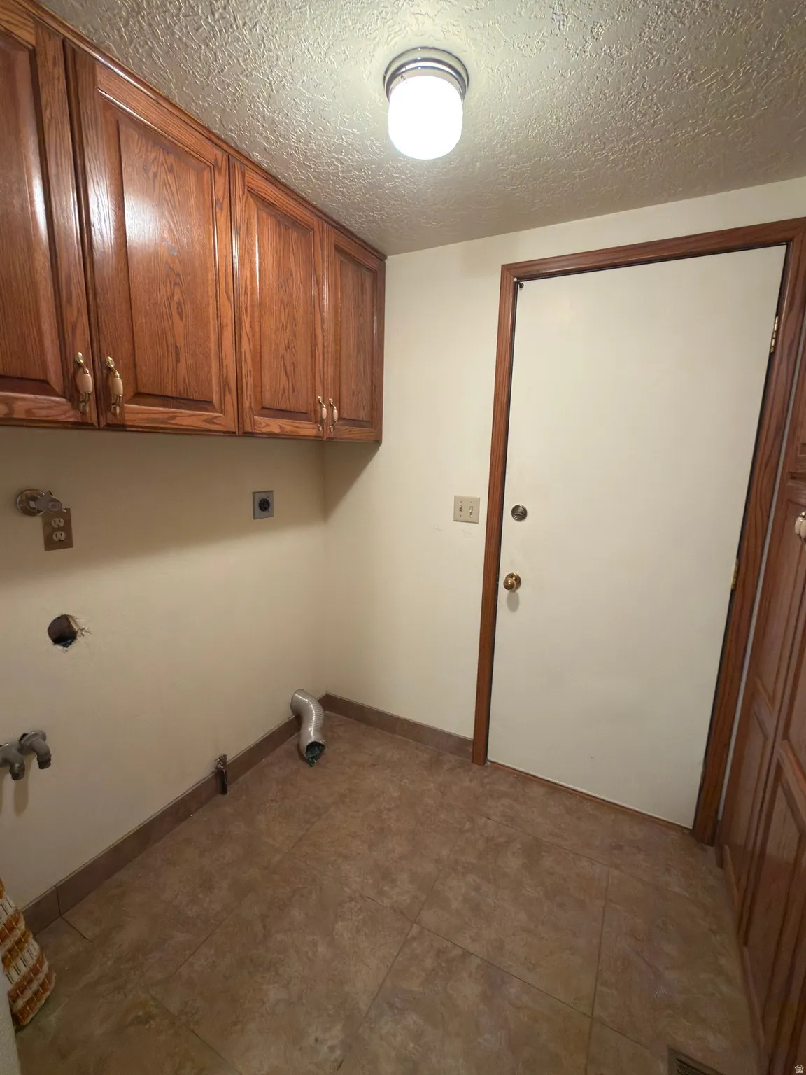Utility space featuring wood-finish cabinetry, tile flooring, a flush-mount ceiling light, and a solid core door with wood-finish trim