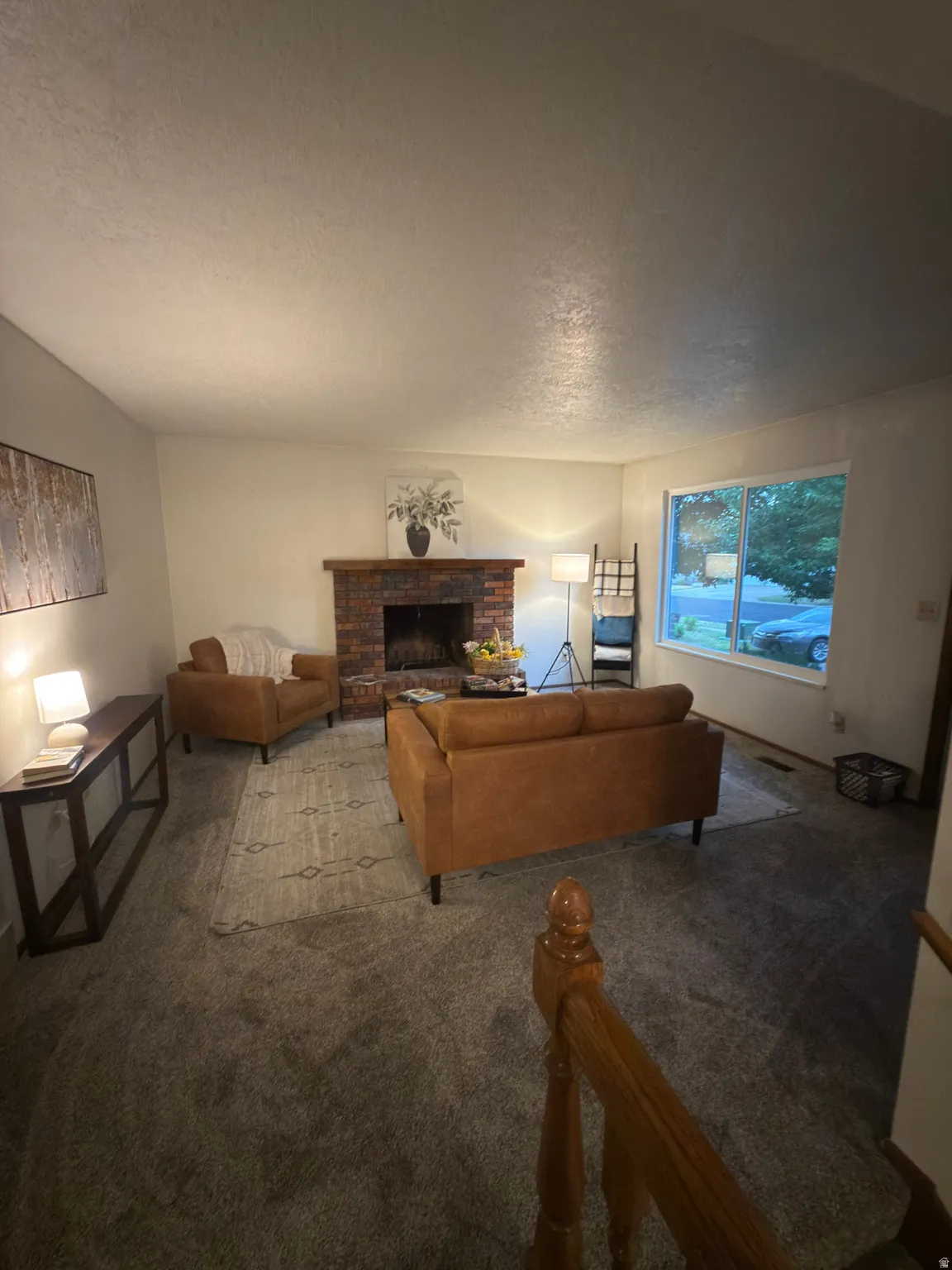 Living area with textured carpeting, a brick fireplace, and a large window
