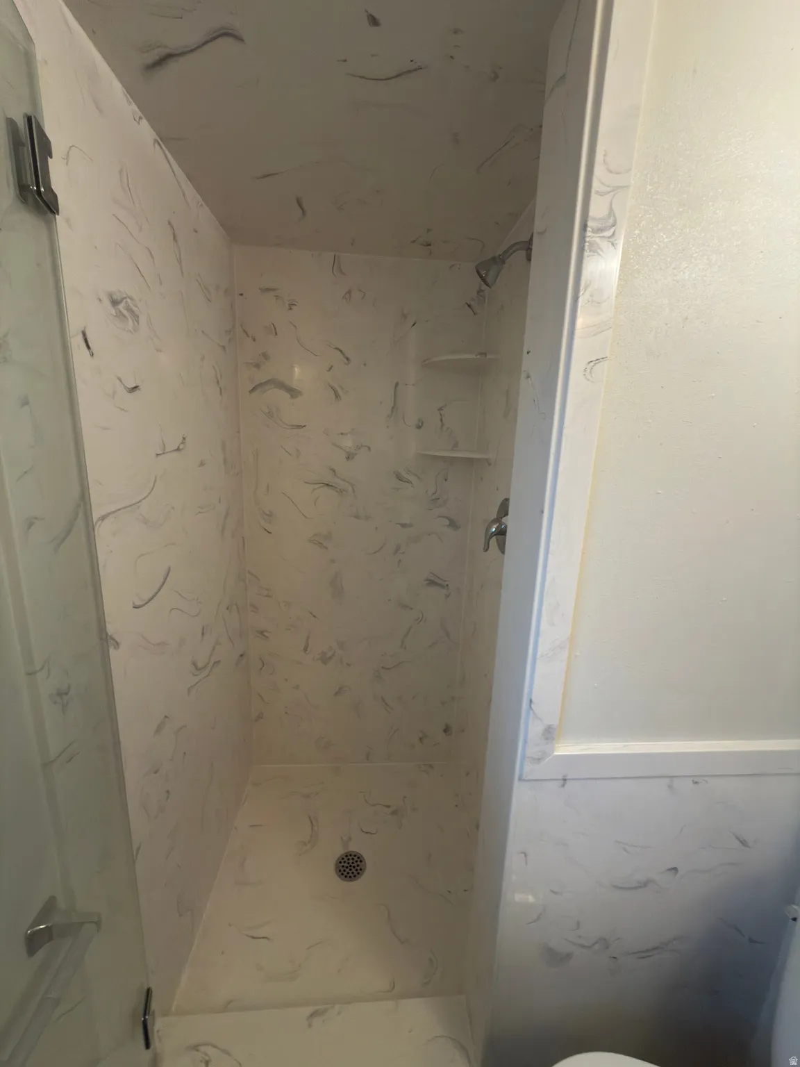 Walk-in shower with a glass enclosure and a patterned white and gray surround