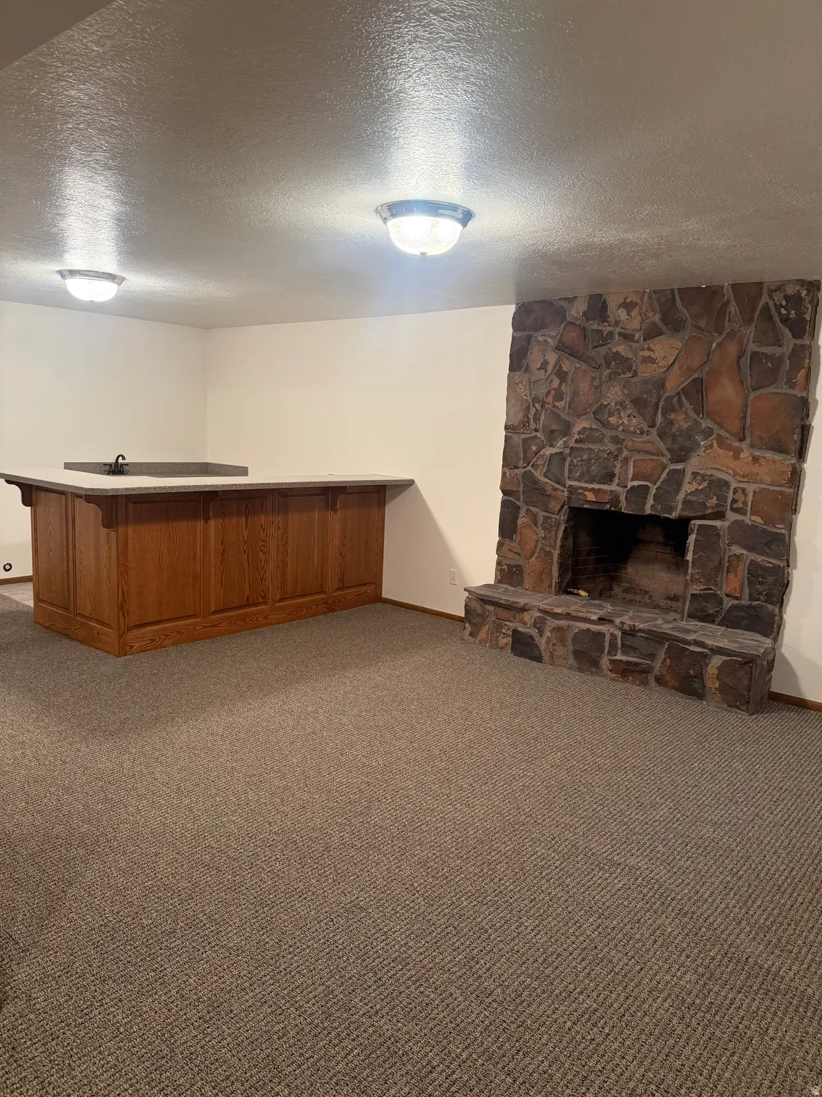 Stone fireplace with hearth and wood-paneled wet bar featuring a solid surface countertop