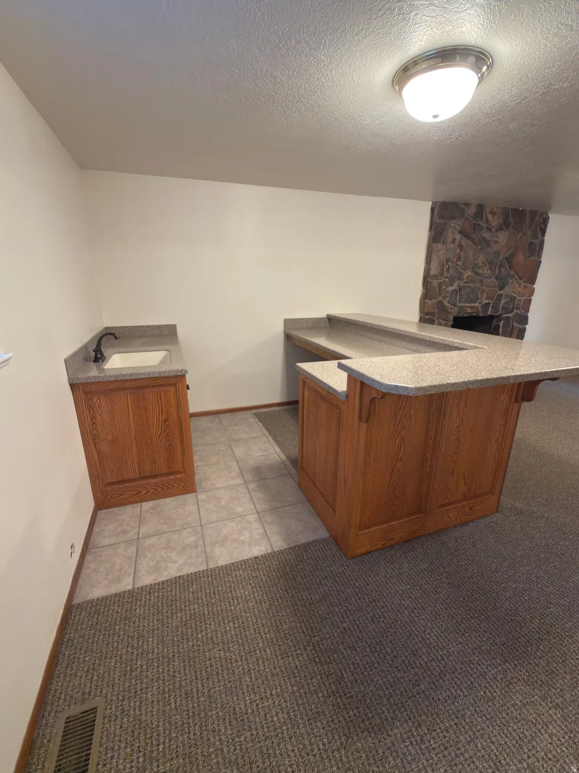 Wet bar with wood cabinetry, light-toned countertop, and undermount sink