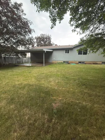 Rear exterior with covered patio, expansive lawn, and mature perimeter trees