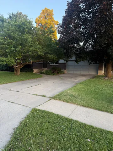 Brick facade residence with an attached garage, mature trees, and a concrete driveway