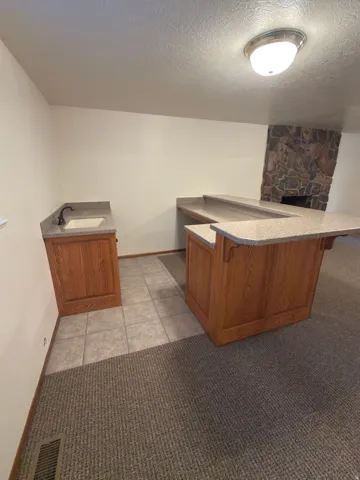 Wet bar with wood cabinetry, light-toned countertop, and undermount sink