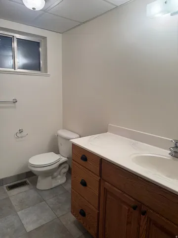 Bathroom featuring a vanity with wood cabinetry, a white countertop with integrated sink, and a commode