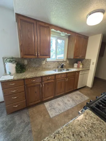 Kitchen featuring wood cabinetry with decorative hardware, granite countertops, tile flooring, and a double basin sink