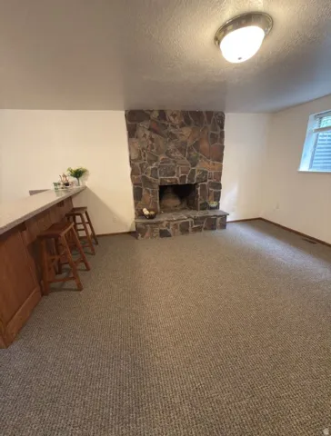 Stone-clad fireplace with hearth, complemented by a wood-paneled bar featuring a light-toned countertop
