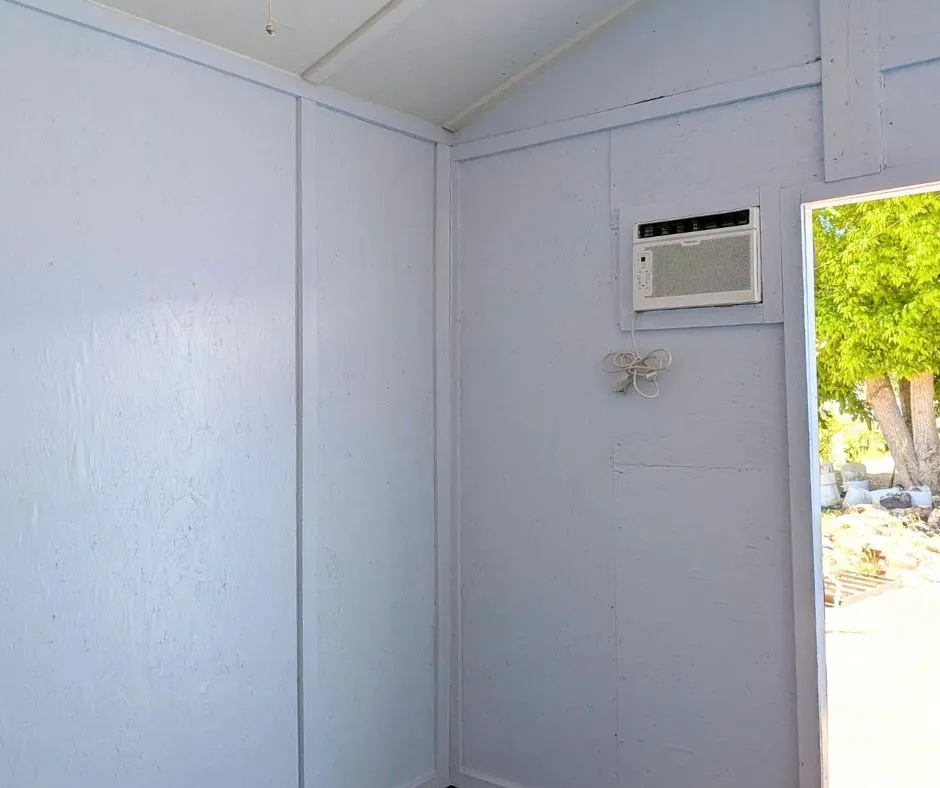 Interior wall featuring a window-mounted air conditioning unit and light-colored paneling
